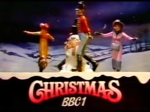 BBC1 Christmas model from 1980. A model of four figures in Victorian dress ice-skating around a snowman with a nighttime background of hills and trees. The two male figures are dressed in soldiers uniforms, the two female figures have bonnets, gloves and muffs. The snowman has a scarf and a top hat. The moon and stars are visible in the sky. the bottom third of the screen has a caption which reads "Christmas BBC1".